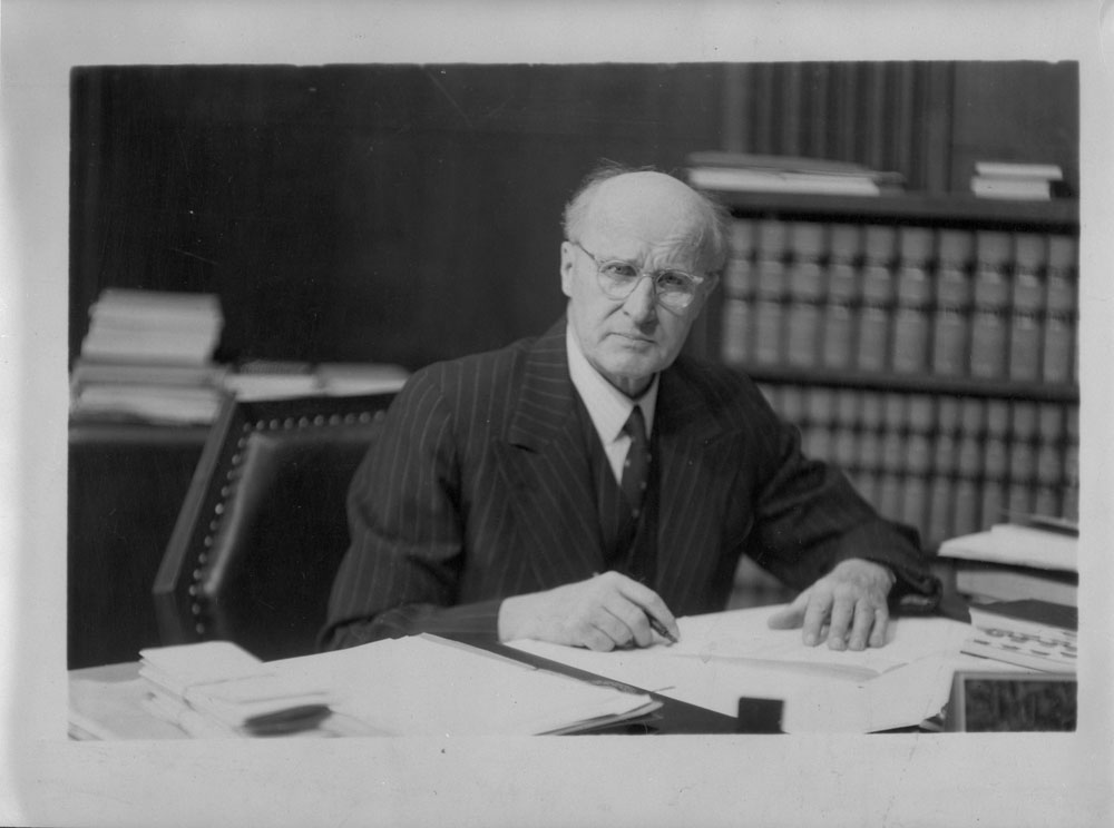 Justive Ivan Rand sitting behind a desk with a book in front of him.